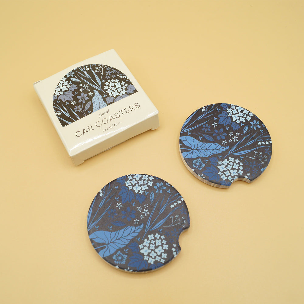 two black car coasters with blue leaves on them are next to a box labeled Car Coasters
