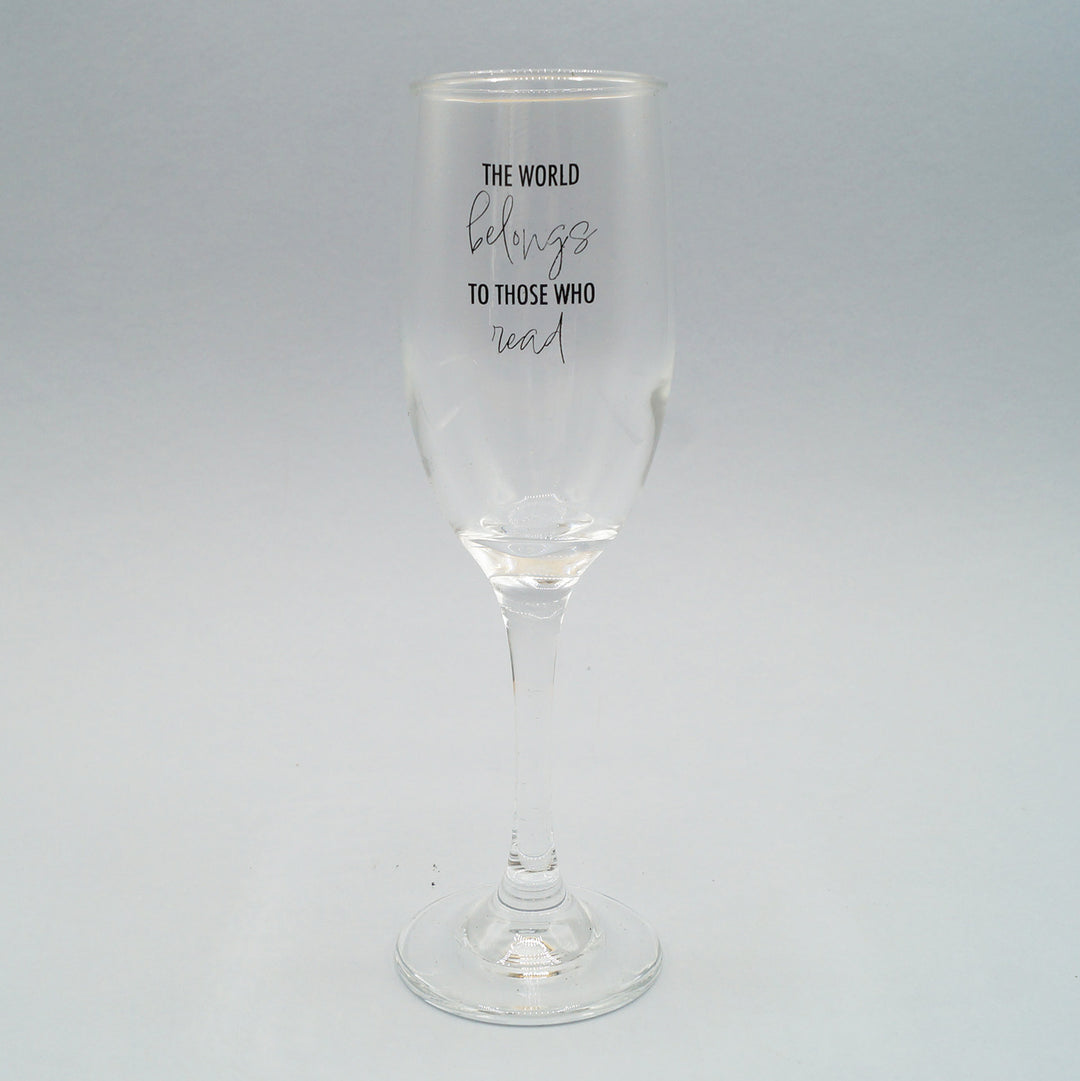 a clear champagne flute with the quote The World Belongs to Those Who Read