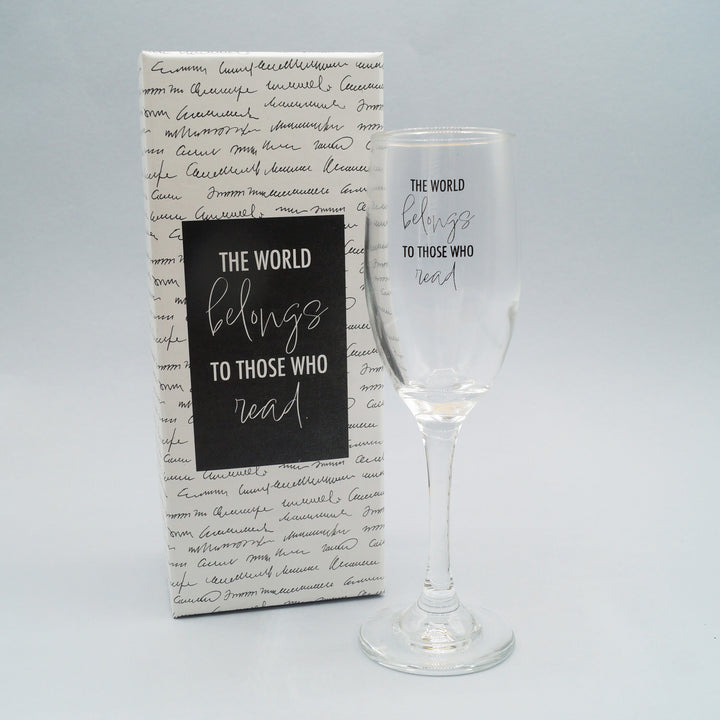 a clear champagne flute with the quote The World Belongs to Those Who Read next to a white box with the same quote on it