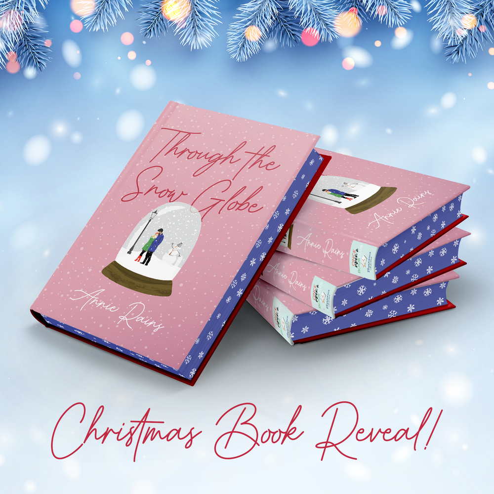 a hardcover copy of a special edition of Through the Snow Globe laying against a stack of 3 other copies. The book is pink with sprayed blue edges with white snowflakes