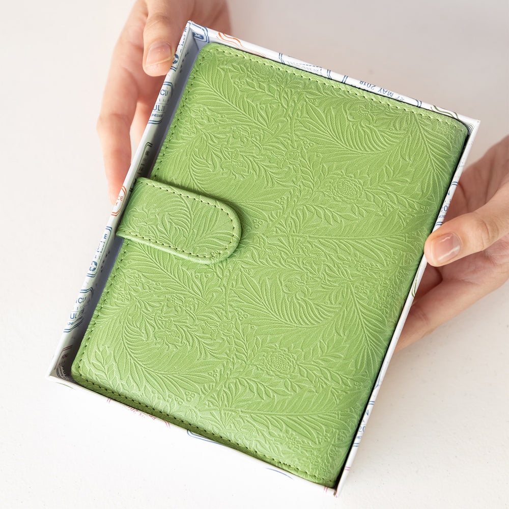 Hands hold an open box that has a green, leaf-patterned planner in it