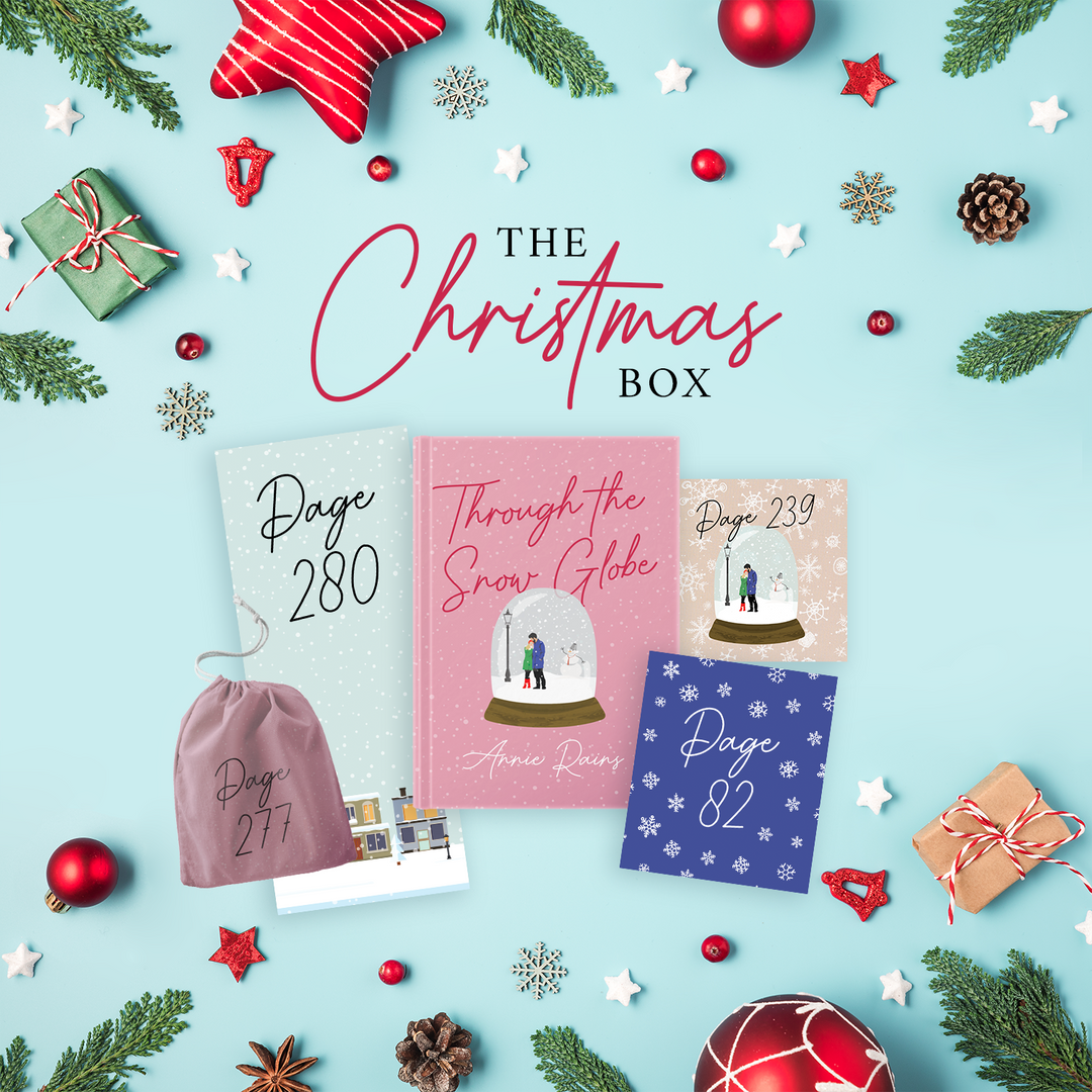 "The Christmas Box" - a pink hardcover special edition of Through the Snow Globe is centered, surrounded by gifts: three boxes and a drawstring bag. The boxes and bags all have page numbers.