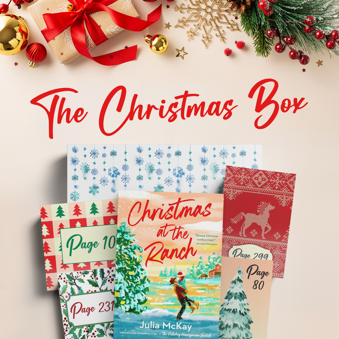 Collection of Christmas-themed packages with festive decorations. The words "The Christmas Box" are in large red font across the middle of the image. The book "Christmas at the Ranch" by Julia McKay is visible on top of the pile of gifts.