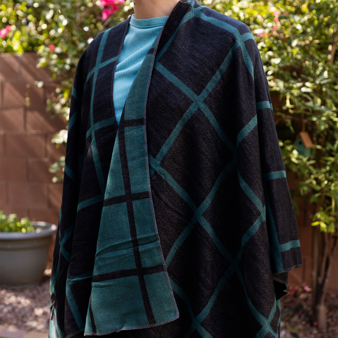 A person wears a reversible dark green and black shawl. One side on the outside is mostly black and green lines crisscrossed across it and the inside is mostly dark green with black lines crisscrossed across it.