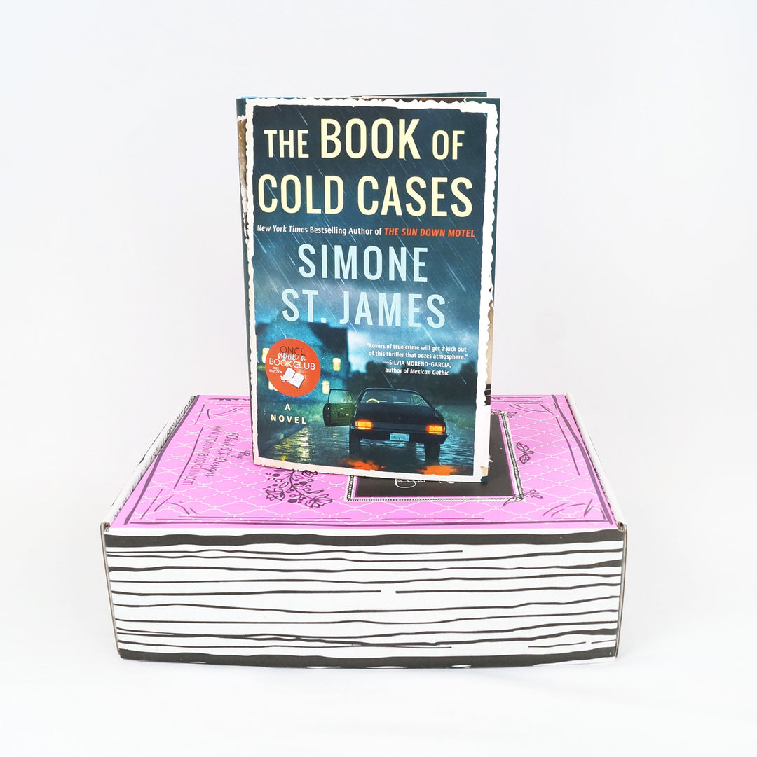 a hardcover edition of The Book of Cold Cases by Simone St James stands on a pink box