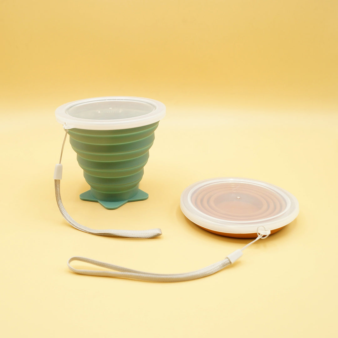 a pair of collapsible cups sit next to each other, the green one on the left is extended and the one on the right is collapsed and flat