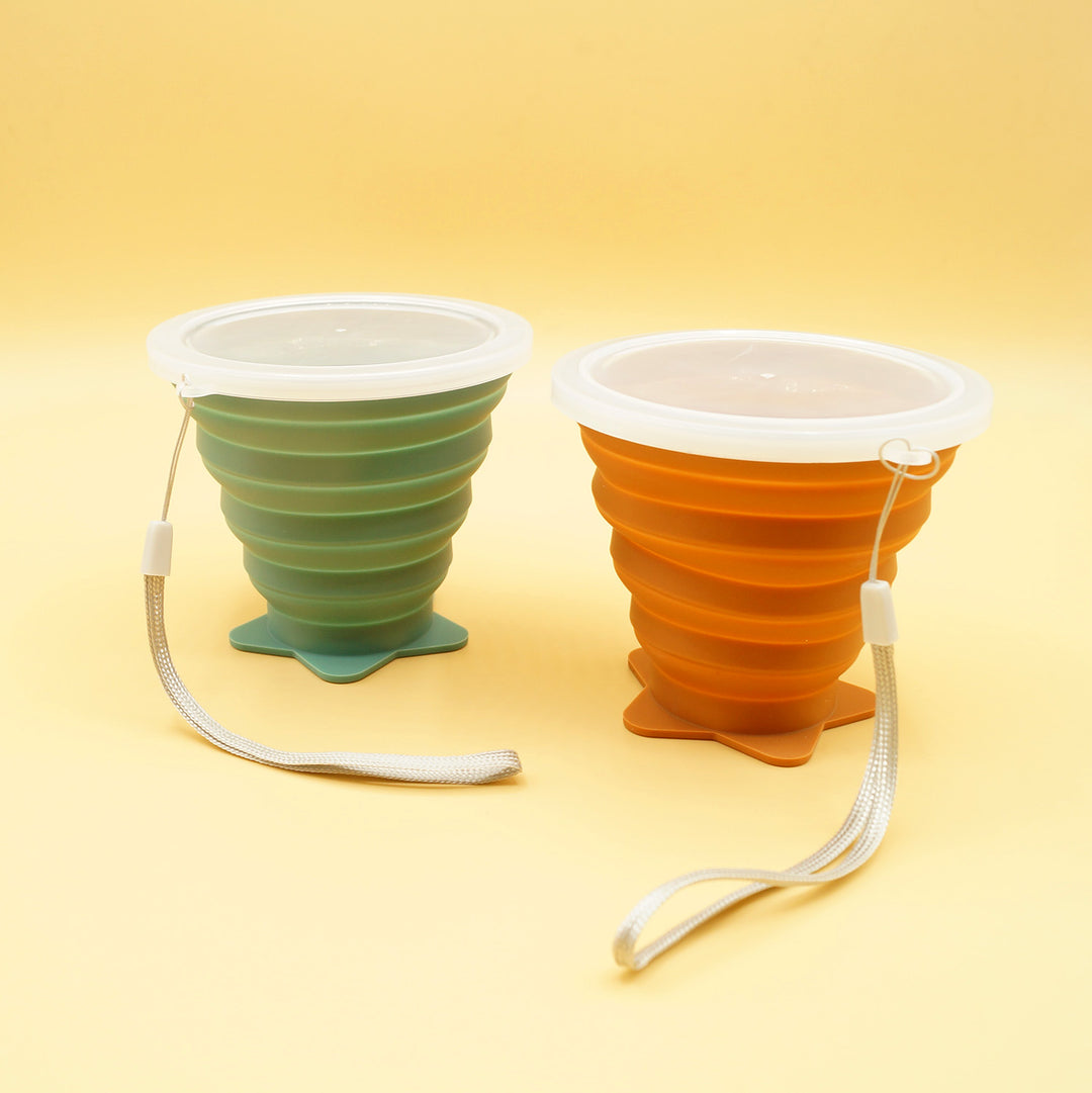 a pair of collapsible cups sit next to each other, one green and one orange, fully extended