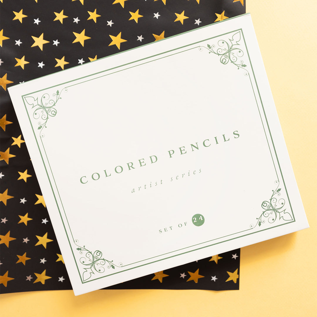 A white box labeled "colored pencils" sits on a black paper with a gold star pattern