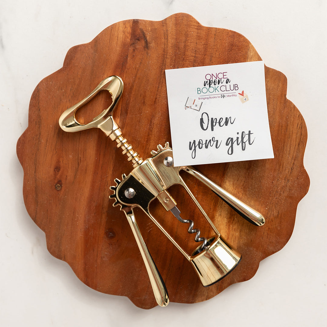 a gold corkscrew wine opener sits on a wood circle with an "open your gift" sticky note