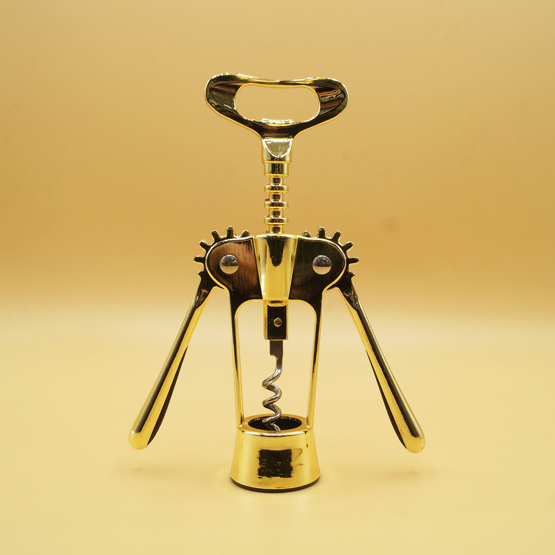 a gold corkscrew wine opener stands in front of a yellow background