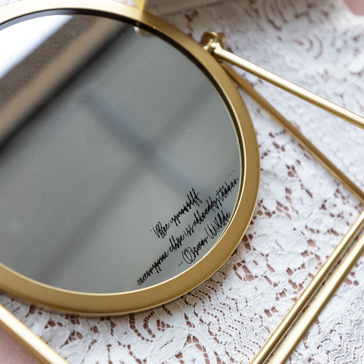 a vanity mirror with gold trim and the quote "Be Yourself, everyone else is already taken" - Oscar Wilde, lays on a white lace background