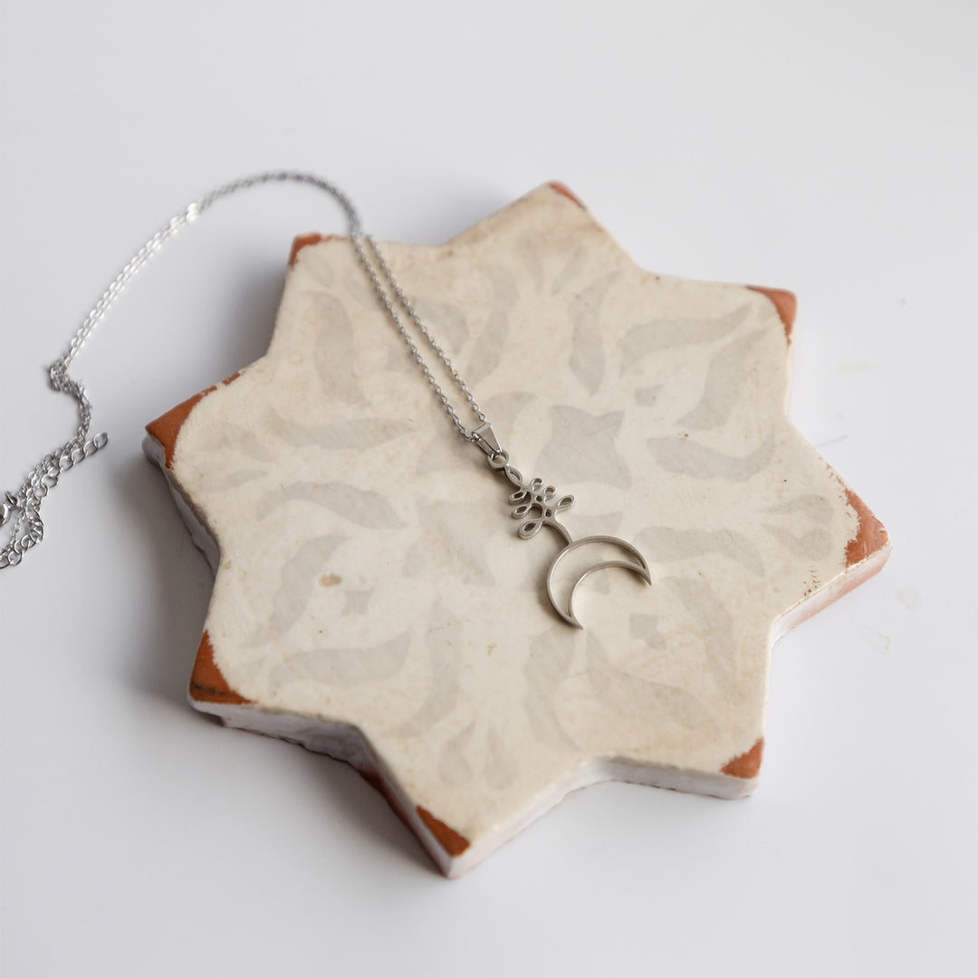 A silver necklace with a crescent moon lays on a star-shaped ceramic piece.