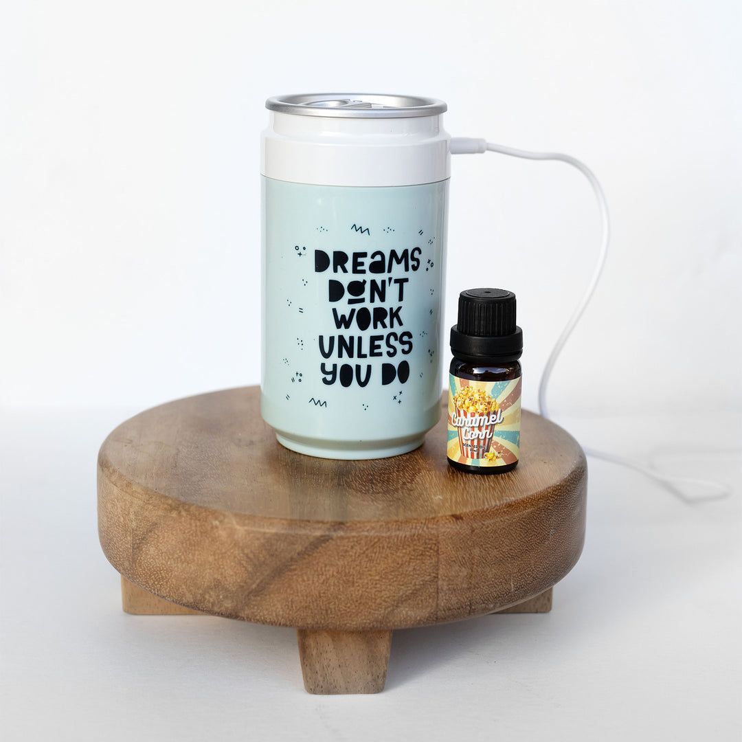 An essential oil diffuser that says Dreams Don't Work Unless You Do next to a small bottle of caramel corn essential oil