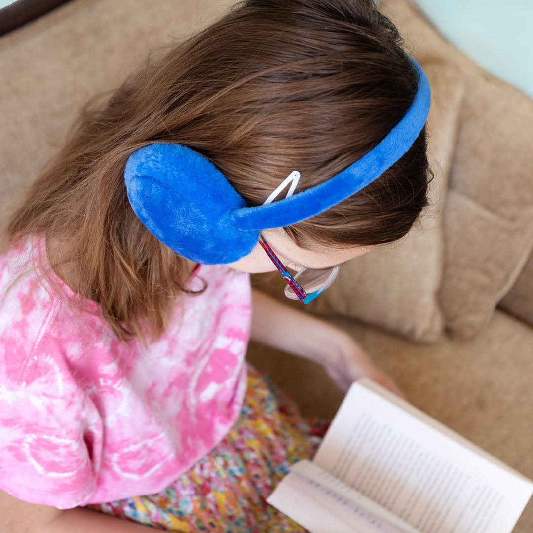 A girl looking down reading is wearing blue fuzzy earmuffs