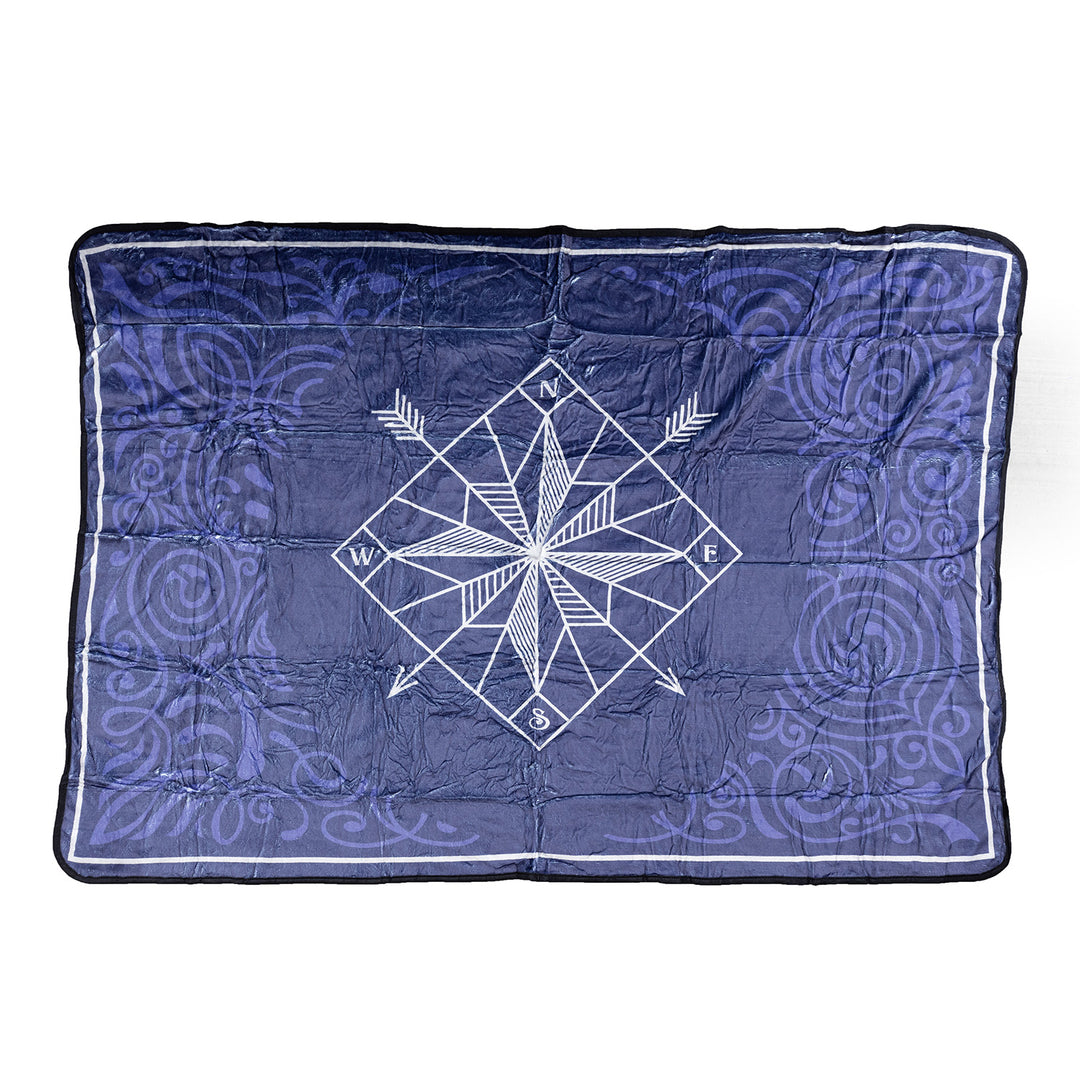 A dark blue fleece blanket with a swirl pattern and a white compass in the middle. The compass has two arrows pointing diagonally down, one southwest and one southeast.