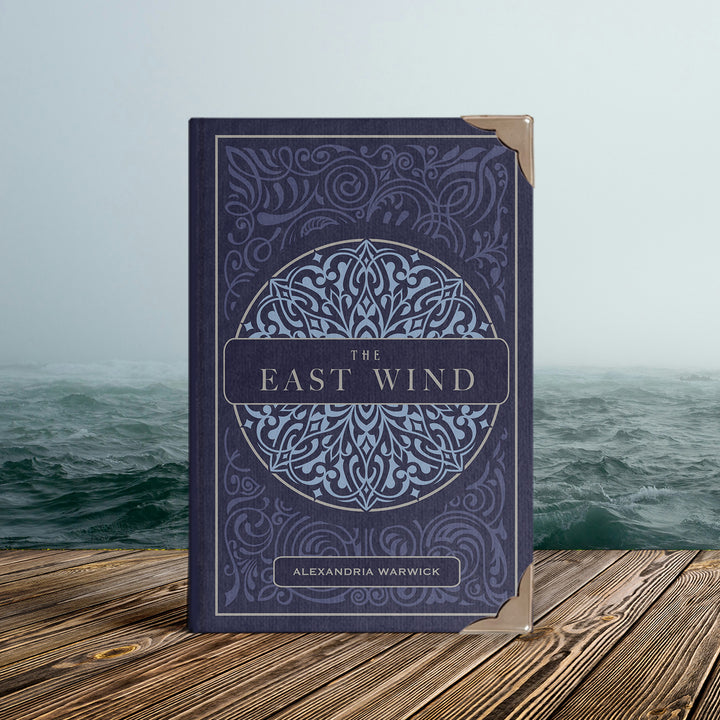 Book titled 'The East Wind' by Alexandria Warwick on a wooden platform with a misty sea background