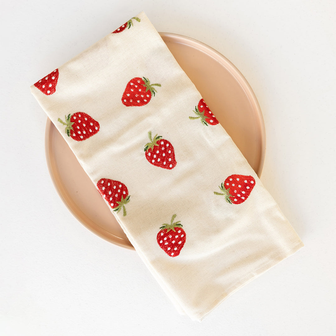 A white tea towel with red embroidered strawberries on it