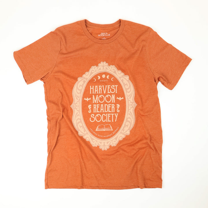 An orange heather short-sleeve t-shirt with a cream-colored graphic on the front that reads 'Harvest Moon Reader Society' inside an ornate oval frame, laid flat on a white background.