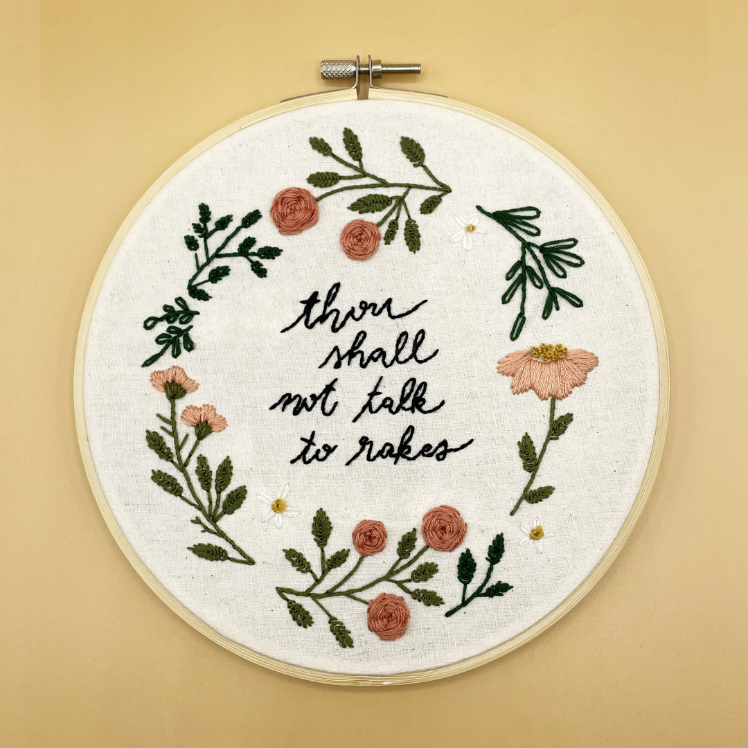 A completed embroidery hoop of small flowers and leaves, and the words "Thou shall not talk to rakes" embroidered in the middle of the hoop.
