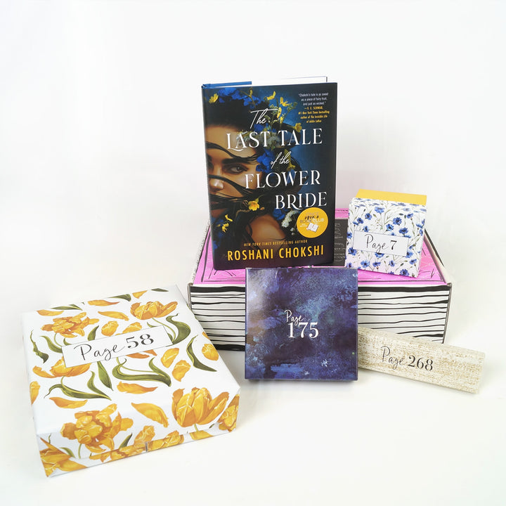 A hardcover edition of The Last Tale of the Flower Bride and a white and blue floral square box are on a pink Once Upon a Book Club box. In front of the box are a yellow and white floral box, blue box, and white box. The boxes all have page numbers.