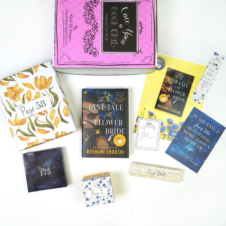 A pink Once Upon a Book Club box is at the top of the image. In front of the box are a yellow and white floral box, blue box, hardcover edition of The Last Tale of the Flower Bride, white and blue floral square box, white box, signature card, bookclub kit, bookmark, and quote card. The boxes all have page numbers.