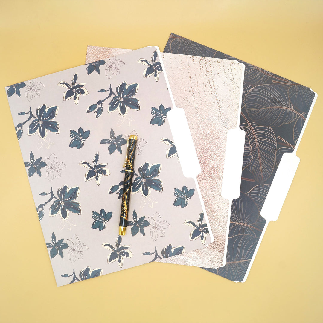 A set of three floral pattern file folders splayed out on a yellow background. A leaf patterned pen sits on top of the folders.