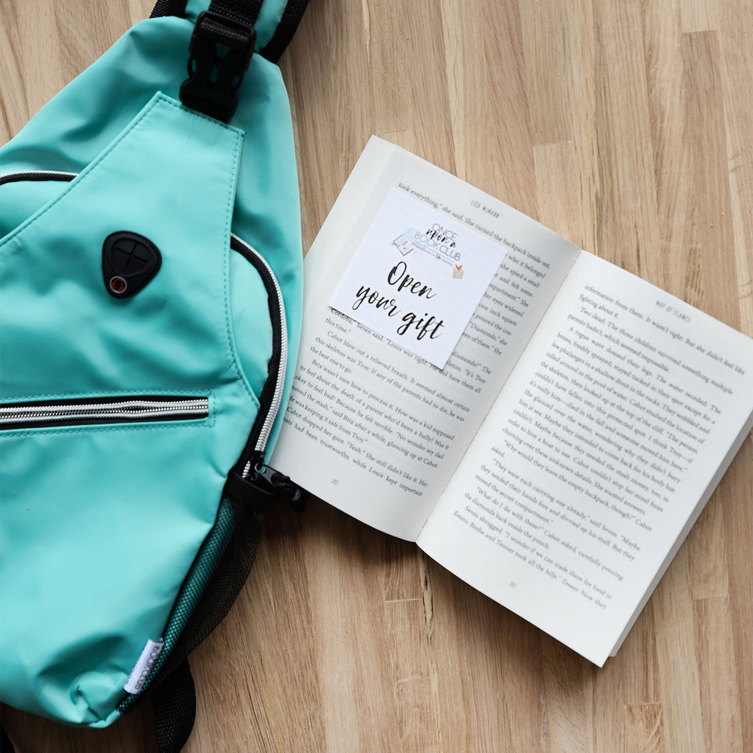 a teal shoulder backpack next to an open book with an open your gift sticker on the left page