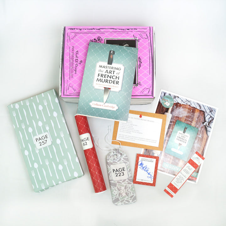A hardcover special edition of Mastering the Art of French Murder lays on a pink box. In front are a rectangular box, red tube, small drawstring bag, recipe card, signature card, bookclub kit, and bookmark. The boxes, tube, and bag all have page numbers.