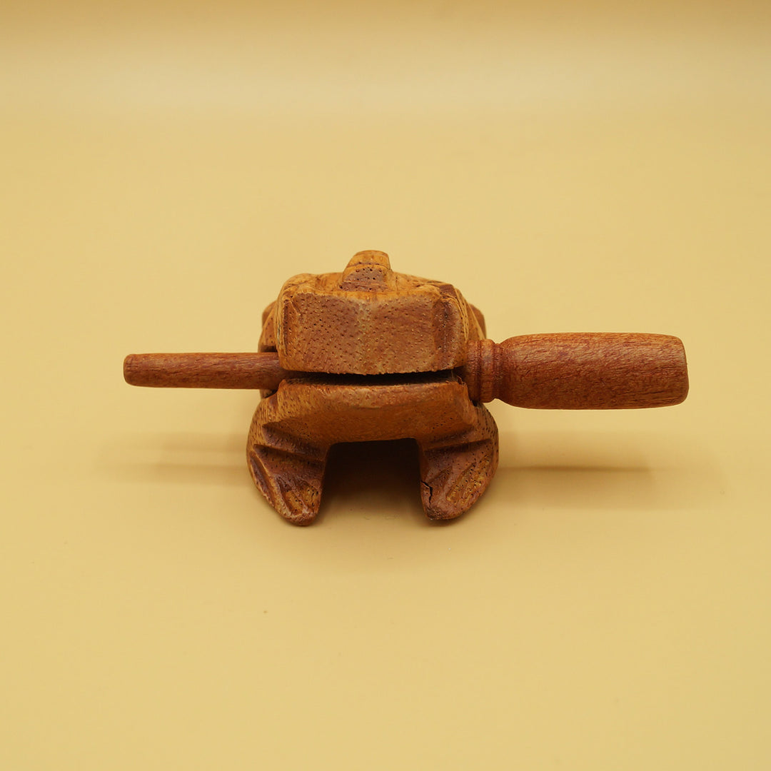 a wooden frog holding a wooden stick in its mouth