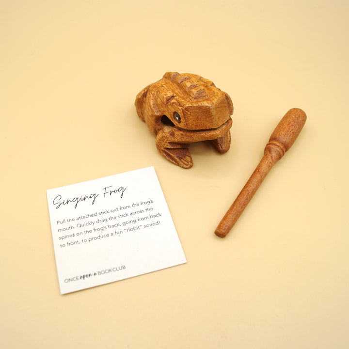 a wooden frog next to a wooden stick and a square piece of paper that says "Singing Frog"