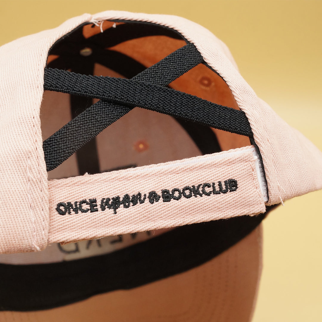 a pale pink baseball cap with an opening in the back for a ponytail. says Once Upon a Book Club on the back