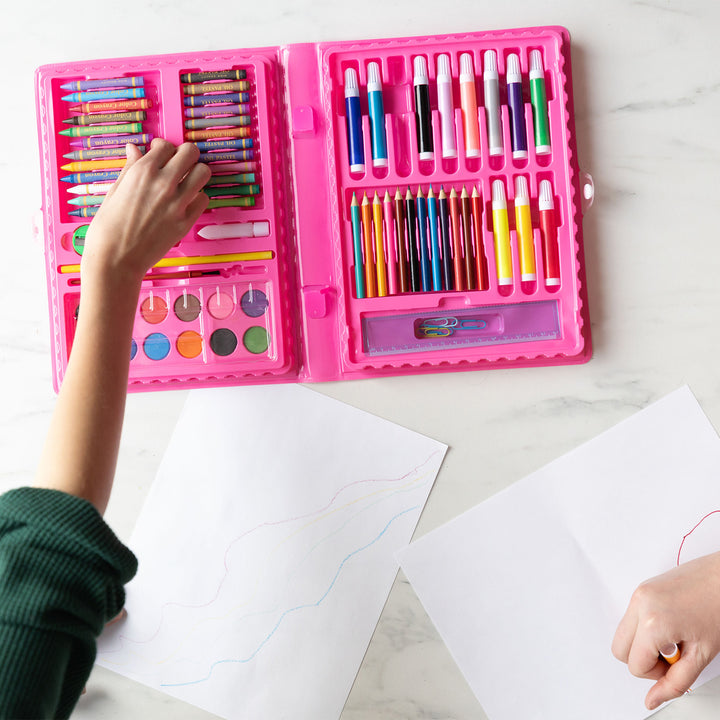 A white hand reaches for a crayon from the art kit as another white hand draws with one of the markers at the bottom of the image. The art kit sits open toward the top of the image.