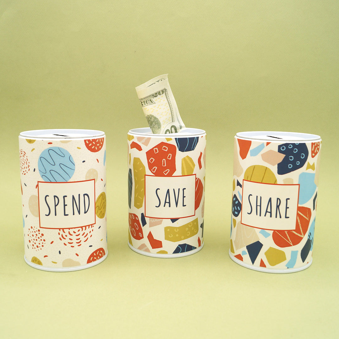The set of 3 money tin sit on a green background. A $20 bill sticks out of the Save jar to demonstrate the slit at the top to practice different money habits.