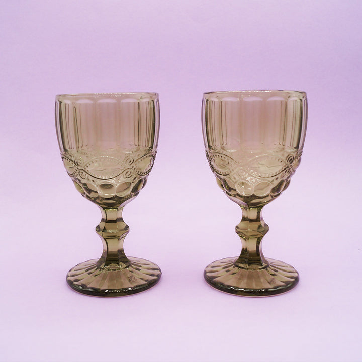 Two green, vintage-style glass goblets on a light purple background