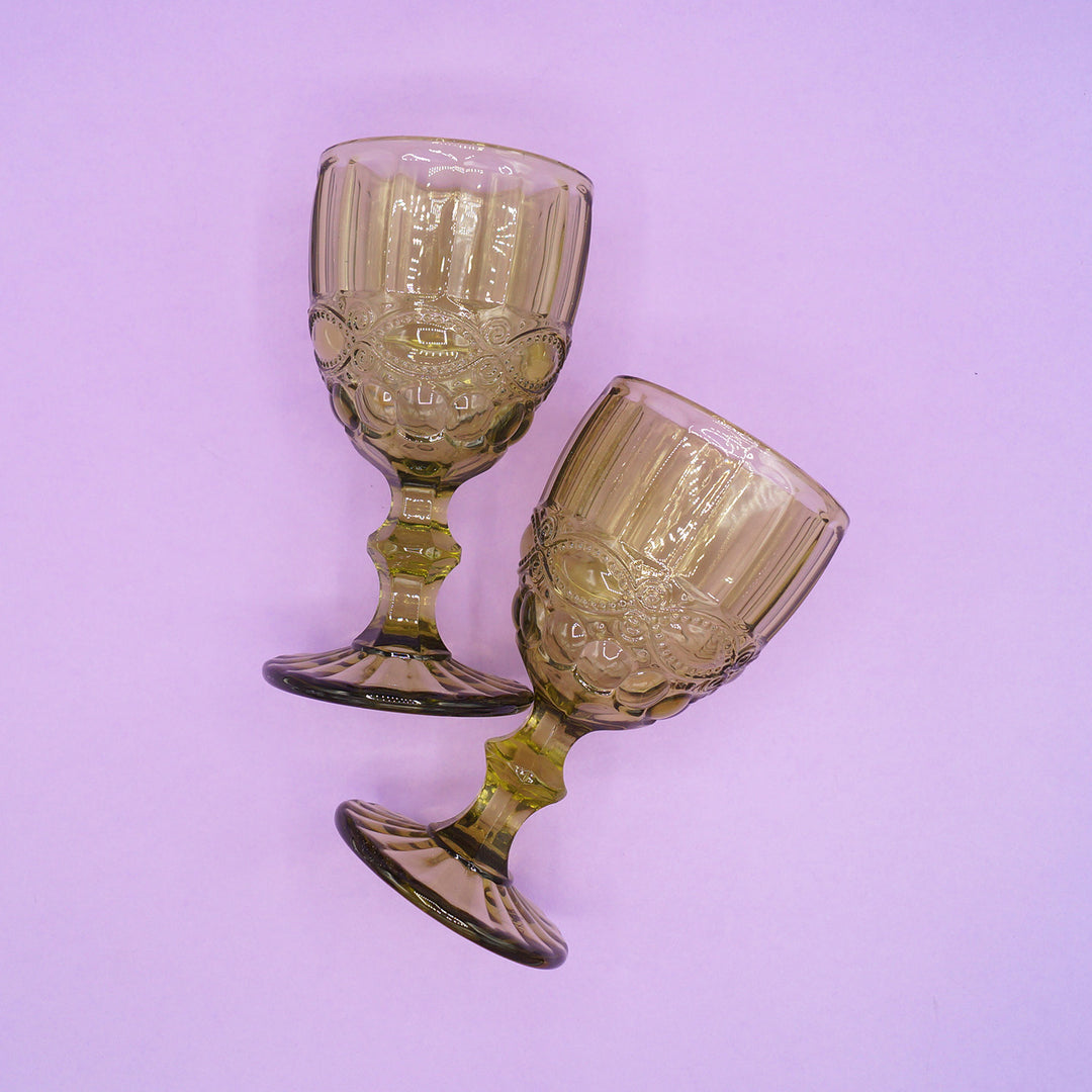 Two green, vintage-style glass goblets on a light purple background