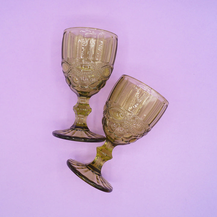 Two green, vintage-style glass goblets on a light purple background