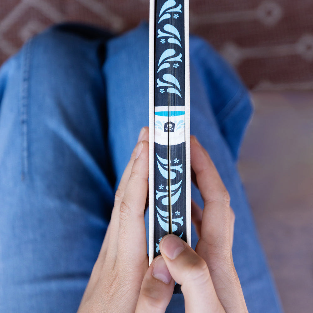 Person holding a copy of Murder at Gulls Nest by Jess Kidd featuring its sprayed page edges