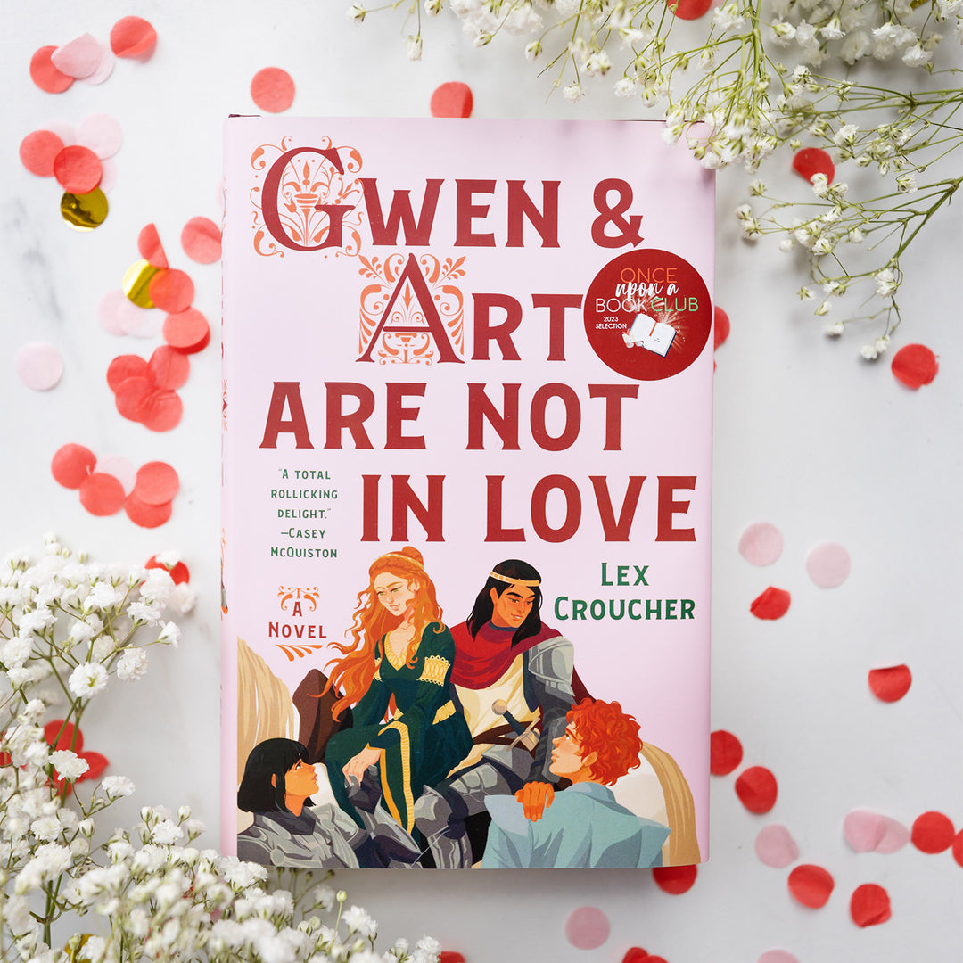 A hardcover copy of Gwen and Art are Not in Love by Lex Croucher on a white background. Confetti and white flowers surround the book.