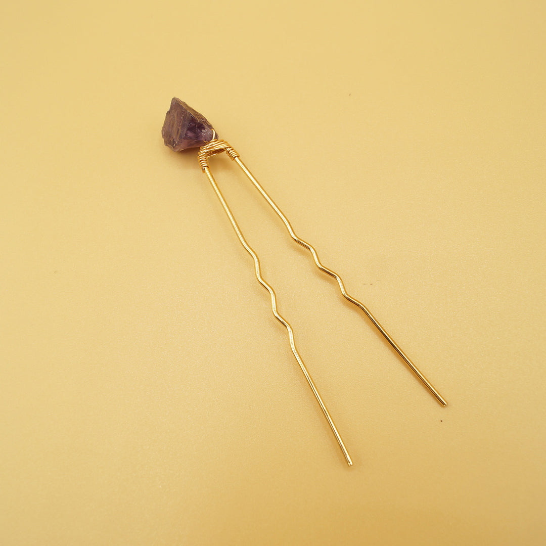 a hair pin lays open with a purple amethyst gemstone on it, against a yellow background