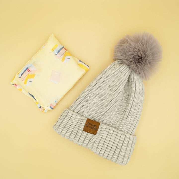 a gray pompom beanie next to a yellow reusable tote bag folded into a square