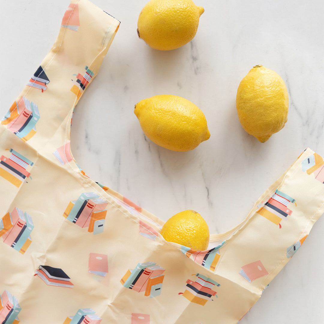 a yellow reusable bag with books printed on it has lemons coming out of the top of it