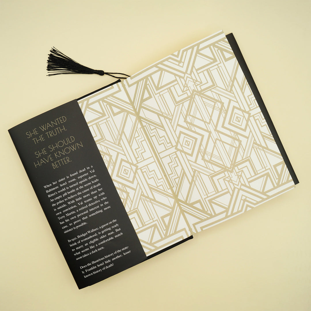 hardcover special edition of Her Sister's Death lays open showing decorative gold and white end papers and a black tassel sticking out from the top middle of the book