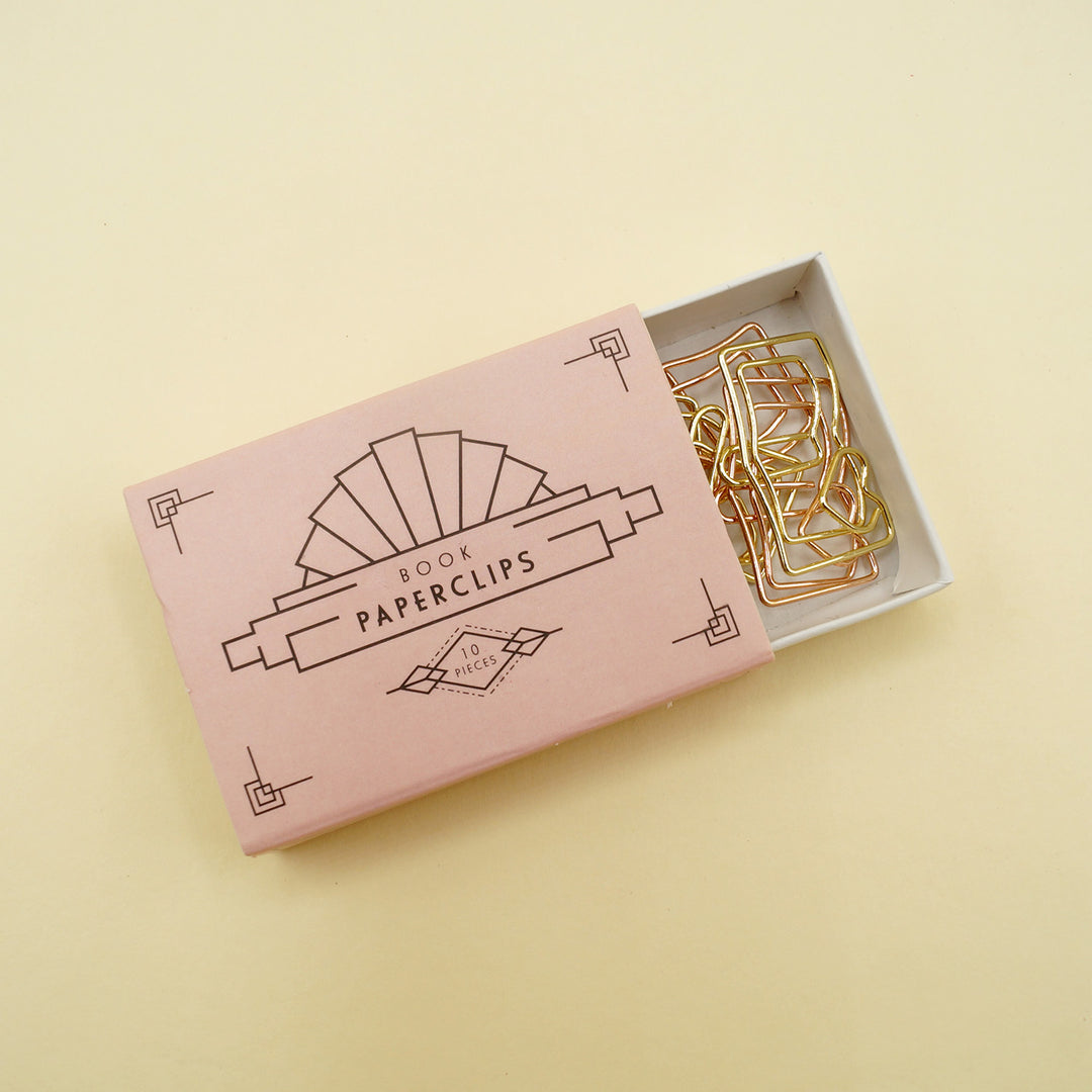 a pink box labeled Book Paperclips 10 Pieces is half open, showing gold and rose-gold book-shaped paperclips inside