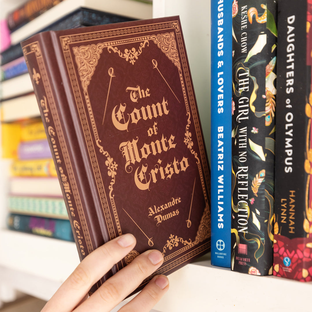 A hand is grabbing a brown book that says The Count of Monte Cristo Alexandre Dumas off of a white shelf next to other books