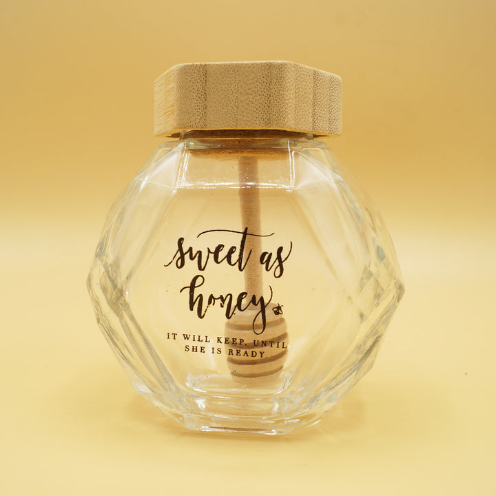 a clear hexagon-shaped honey jar with the words "sweet as honey. it will keep until she is ready" printed on the side