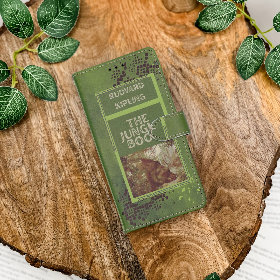 Green book-shaped phone case titled 'The Jungle Book' by Rudyard Kipling on a wooden surface with leaves.