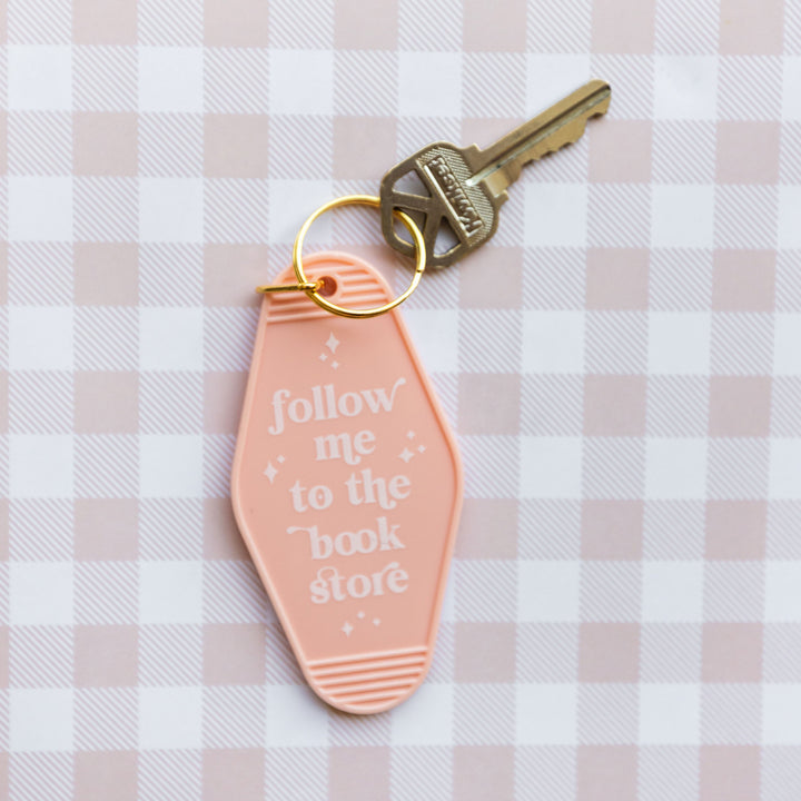 a light peach keychain that says "follow me to the book store" in white writing attached to a golden key