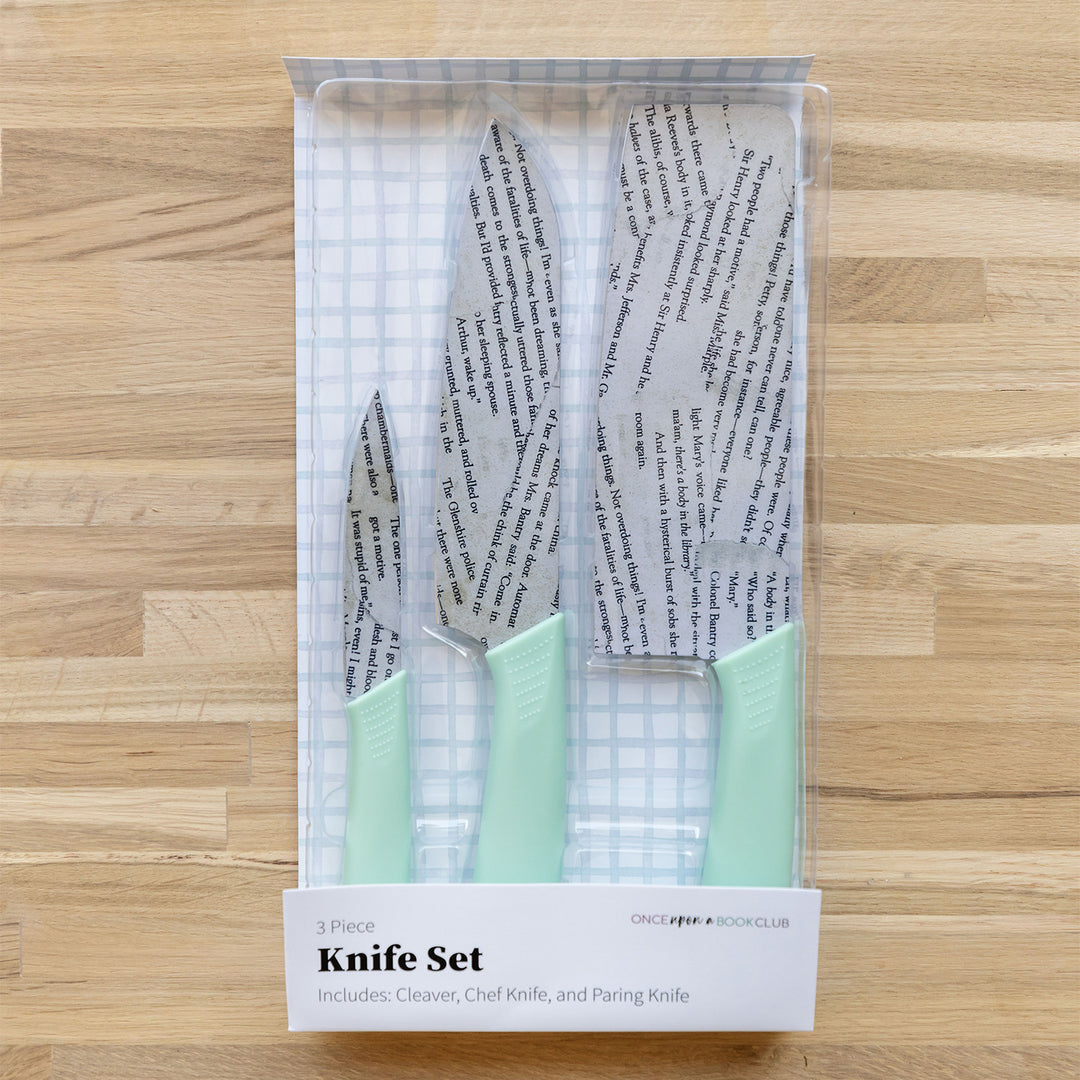 a set of three kitchen knives with seafoam green handles on a wooden table. The blades look like pages have been pasted onto them