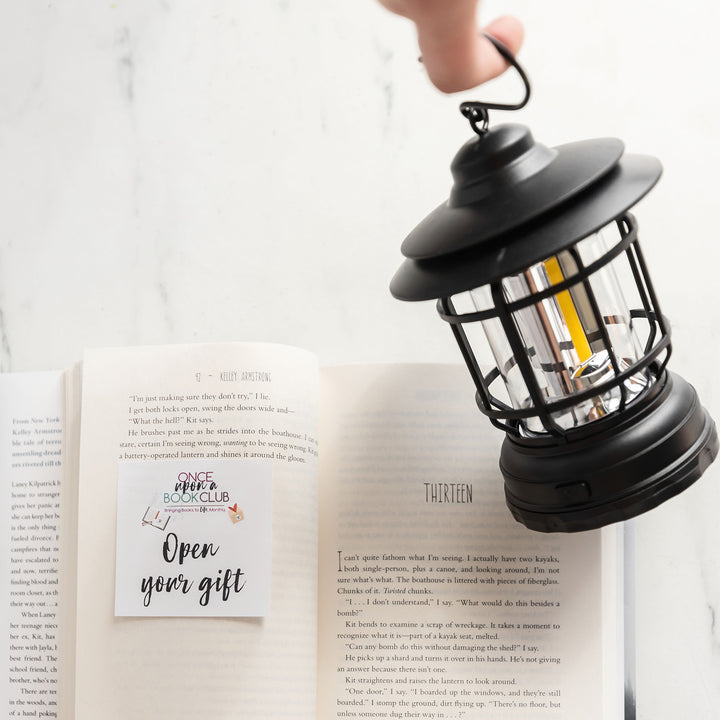 a white hand holds a black hanging lantern over an open book that has an open your gift sticker on the left page