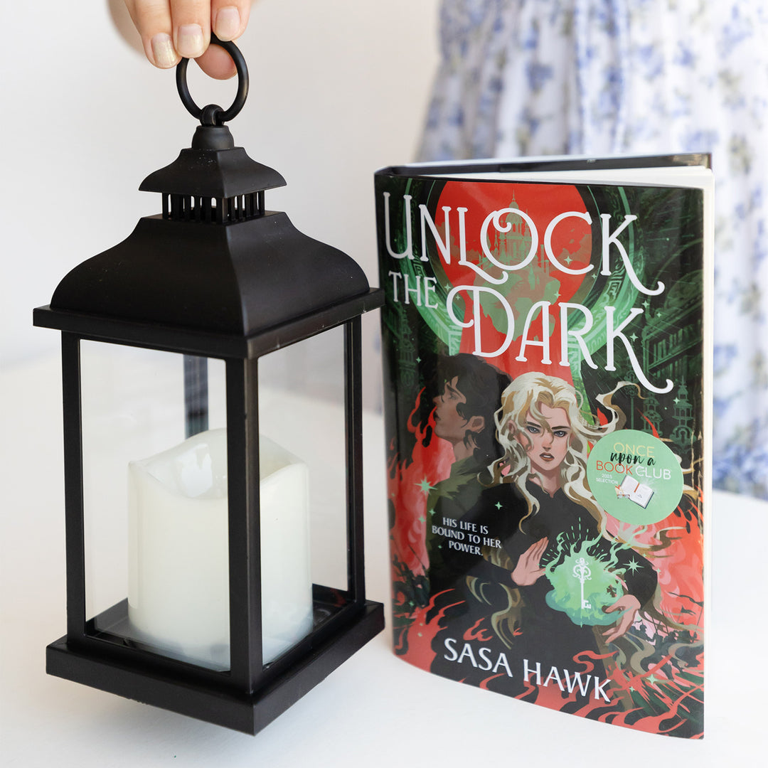 A hardcover edition of Unlock the Dark next to a black lantern with a fake white candle in it.